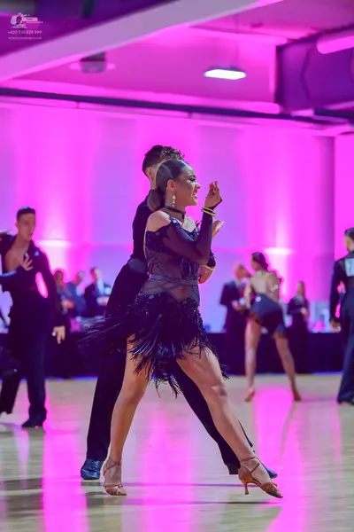 Dancesport competitor: Foreground female dancer: black latin dress with a sheer mesh bodice and a black