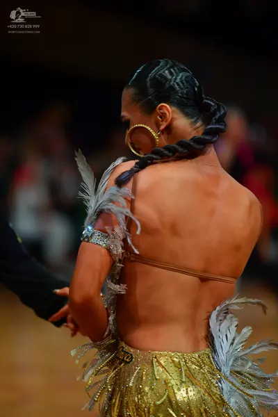 Dancesport competitor: Female dancer: gold sequined backless latin dress with white/grey feather accent