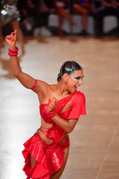 Dancesport competitor: Female dancer: red Latin dance dress with cutouts, featuring a shiny/sequined fa