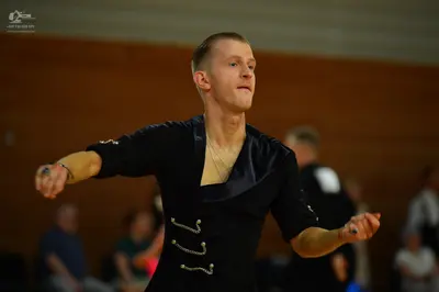 Dancesport competitor: Male dancer: black latin dance top with a v-neck and white decorative embellishm