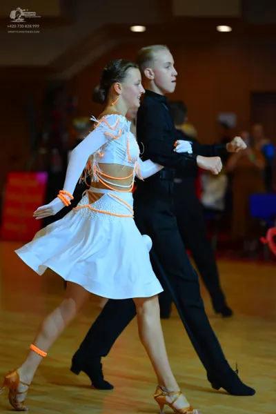 Dancesport competitor: Female dancer: white latin dress with orange-colored decorative straps and bands