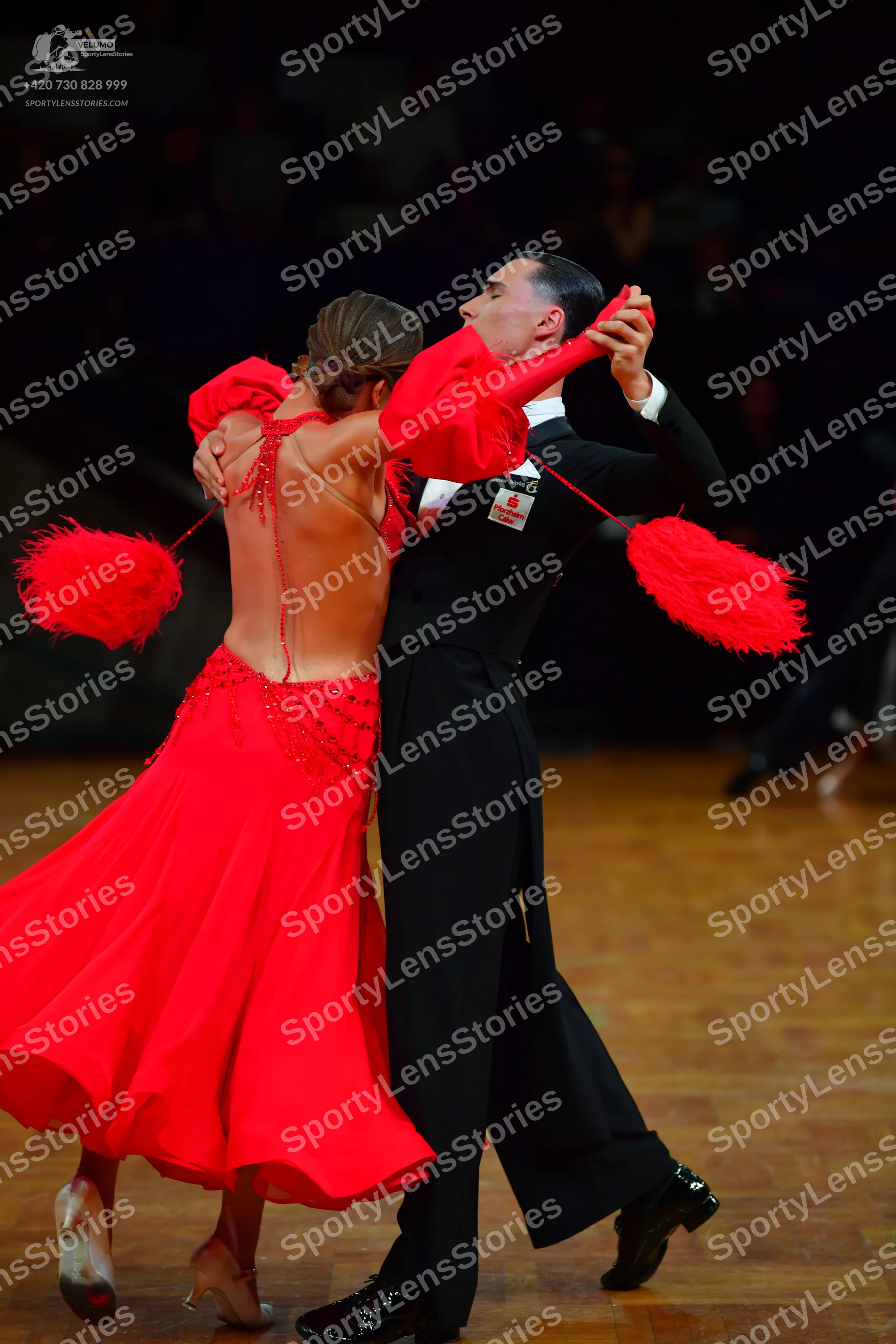 Dancesport competitor: Female dancer: red ballroom dress with a low back, featuring large red fluffy or