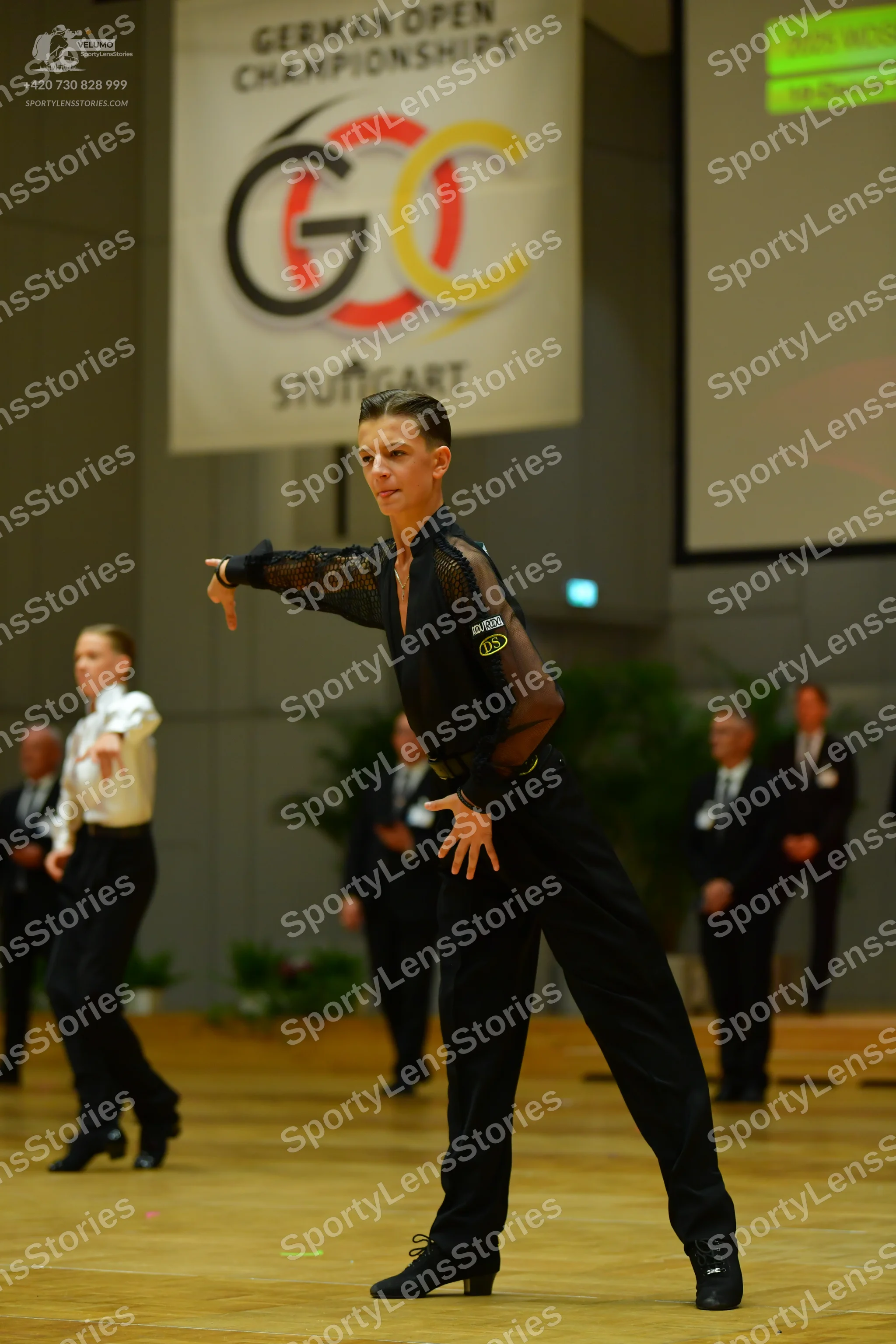 Dancesport competitor: Foreground dancer: black long-sleeved top with mesh sleeves and black trousers