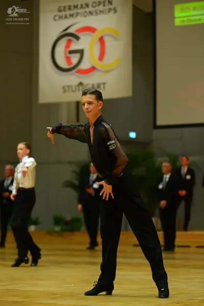 Dancesport competitor: Foreground dancer: black long-sleeved top with mesh sleeves and black trousers