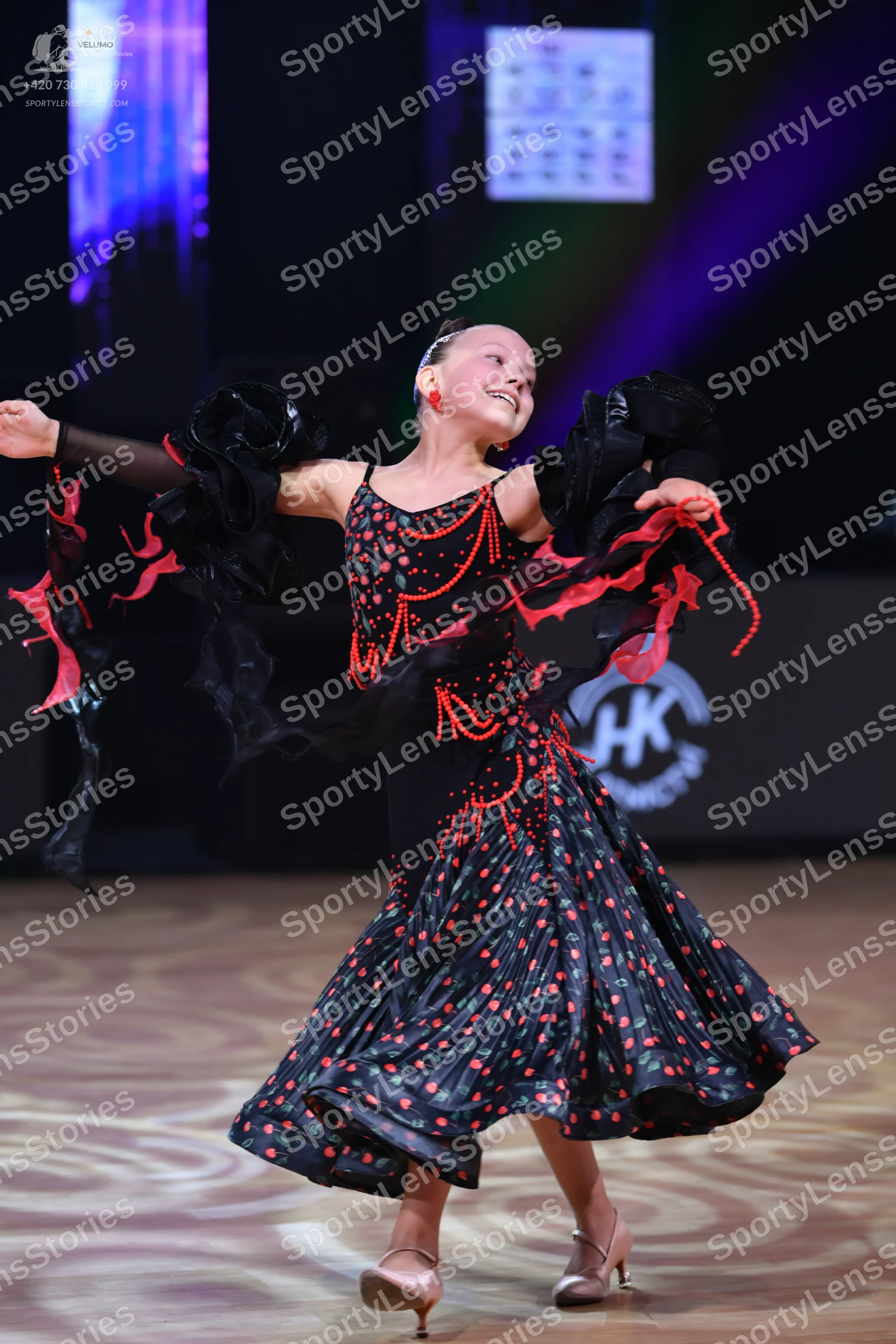 Dancesport competitor: Female dancer: black dress with red patterns, featuring large black ruffled slee