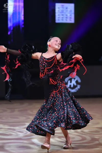 Dancesport competitor: Female dancer: black dress with red patterns, featuring large black ruffled slee