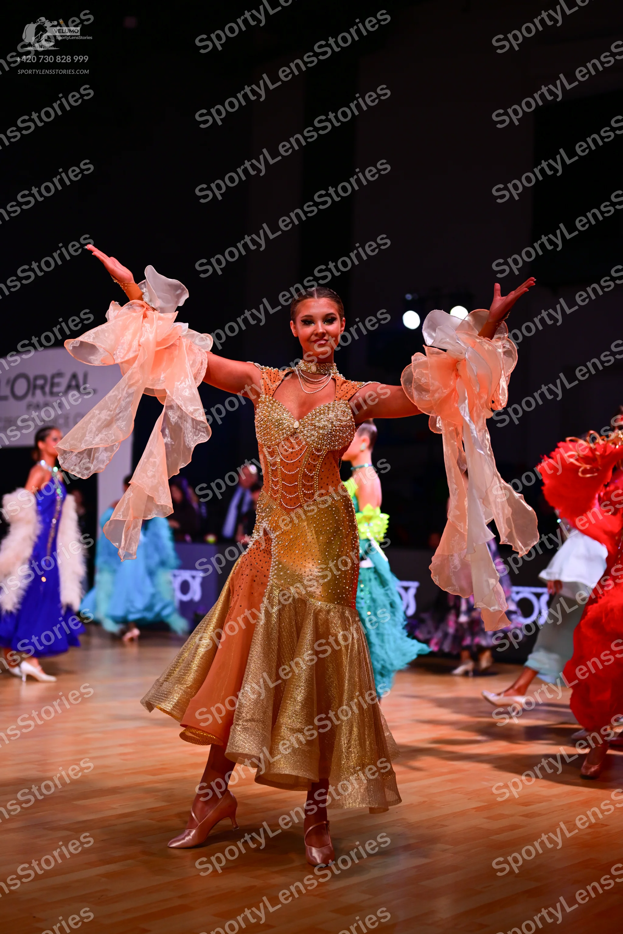 Dancesport competitor: Female dancer in center: gold sequined latin dress with large, sheer, peach-colo
