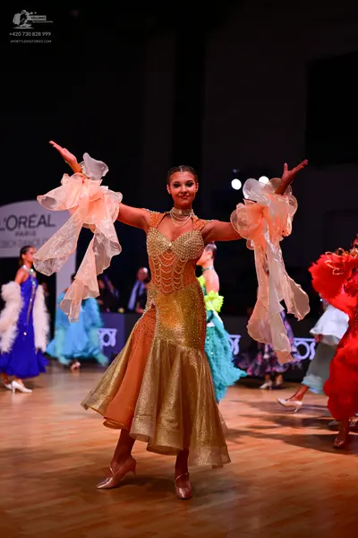 Dancesport competitor: Female dancer in center: gold sequined latin dress with large, sheer, peach-colo