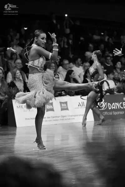 Dancesport competitor: Female dancer (foreground): light-colored latin dance dress with heavy sequin em