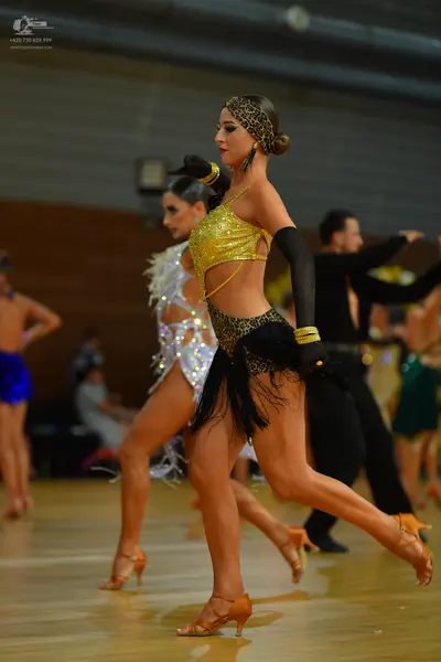 Dancesport competitor: Female dancer in foreground: gold sequin crop top, leopard print bottoms with bl