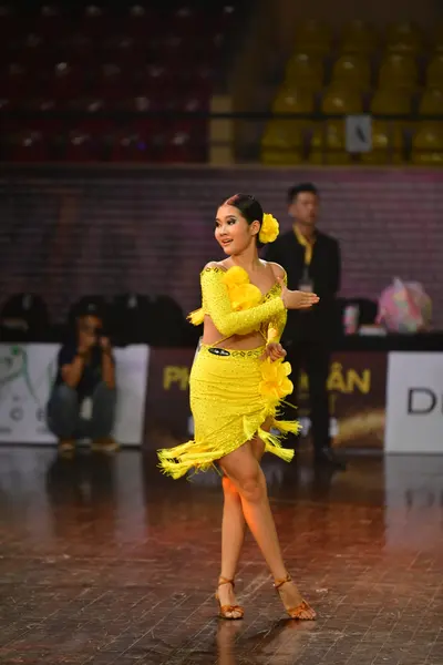 Dancesport competitor: Female dancer: bright yellow Latin dance dress with many ruffled layers and larg