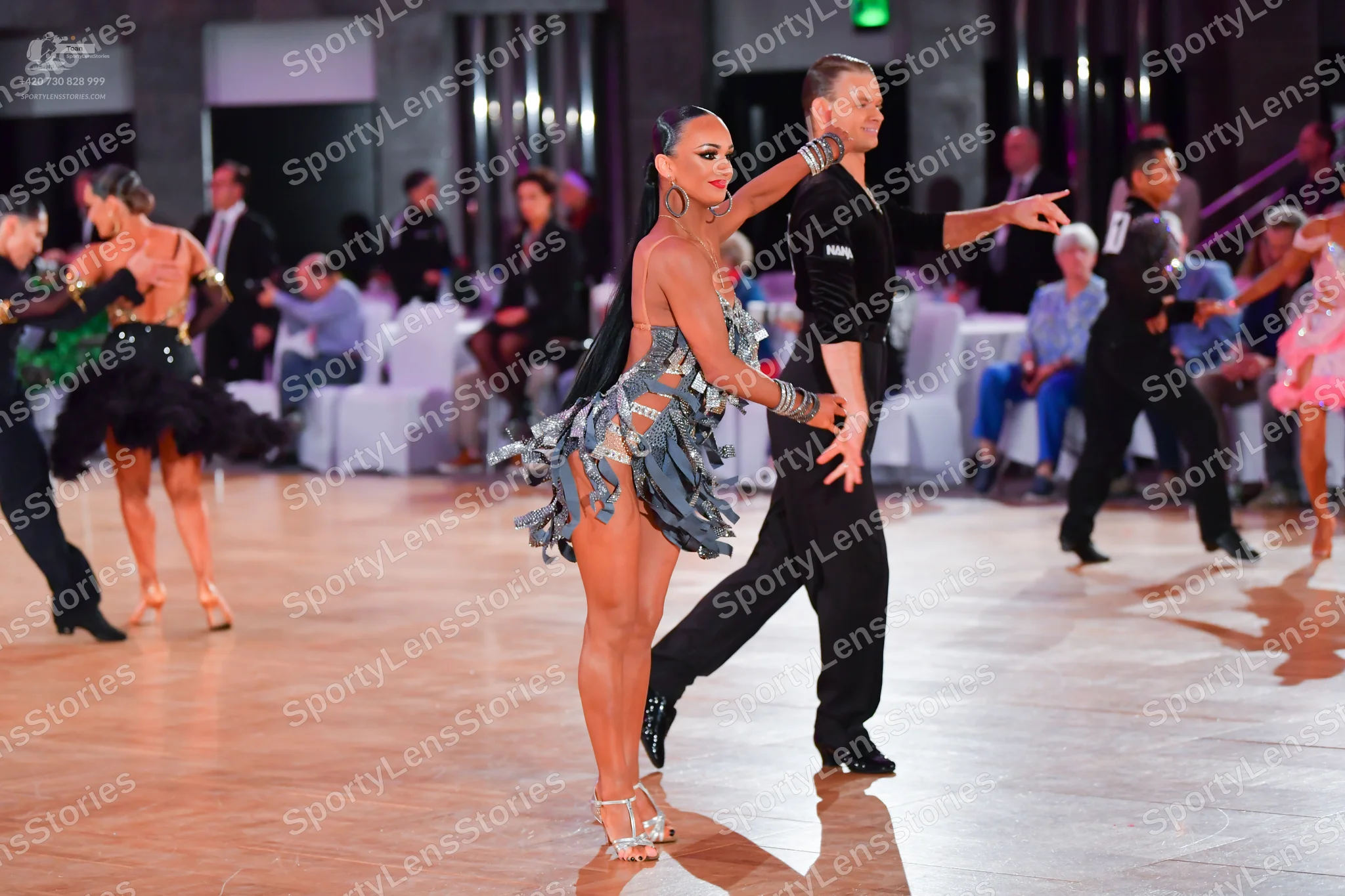 Dancesport competitor: Female dancer (center): grey-blue latin dress with fringe and sequins, large hoo