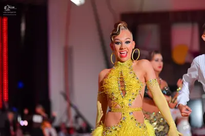 Dancesport competitor: Female dancer in foreground: yellow latin dress with sequins and cut-outs, with 
