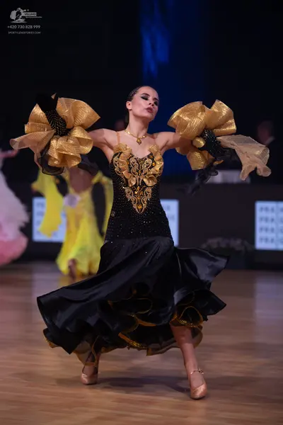 Dancesport competitor: Female dancer: black Latin dress with gold sequin patterns on the bodice, a volu