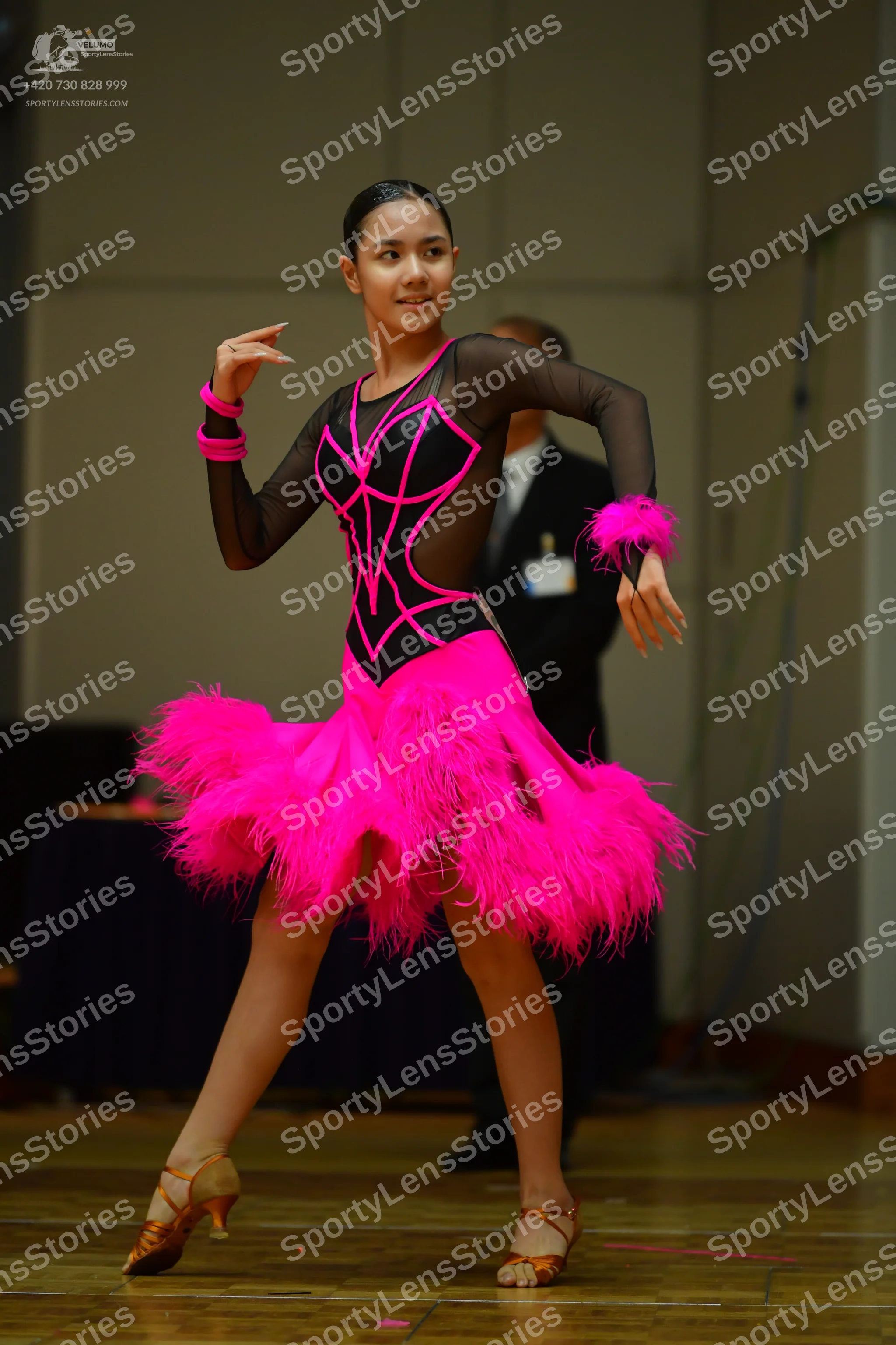 Dancesport competitor: Female dancer: hot pink and black Latin dress with long sheer black sleeves, pin