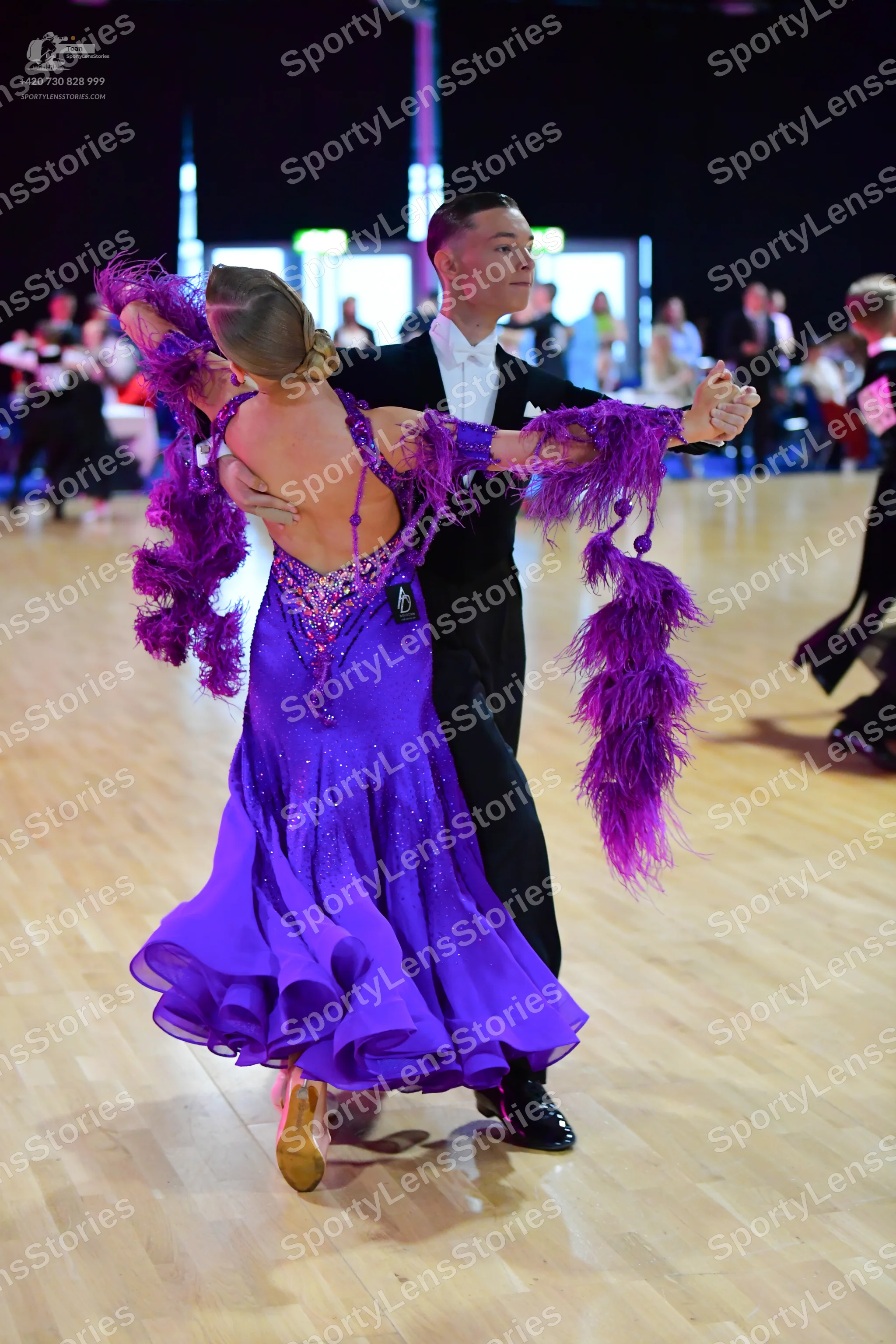 Dancesport competitor: Female dancer: purple ballgown with a sequined bodice and large purple feather d