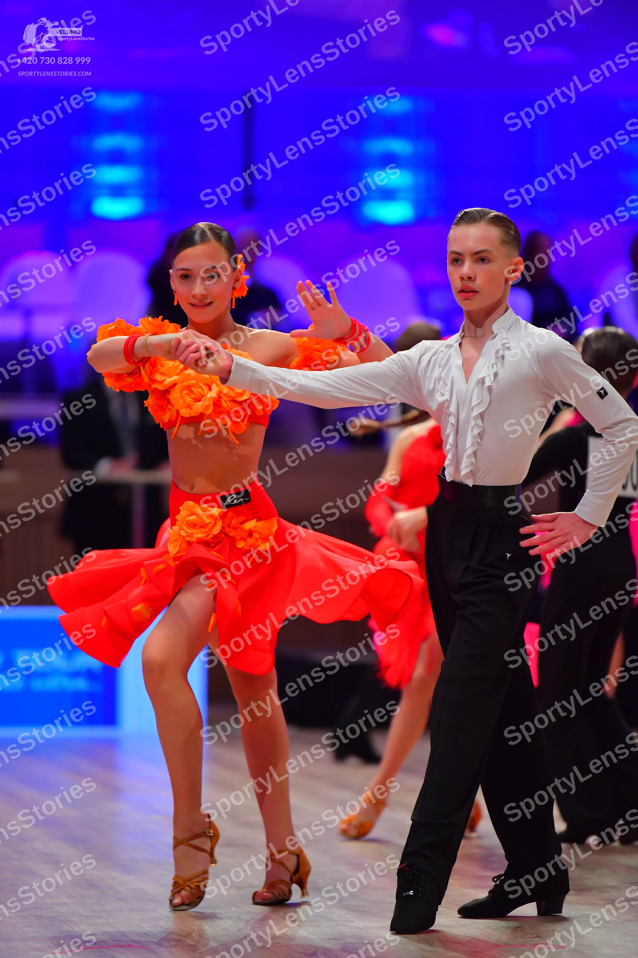 Dancesport competitor: Female dancer: bright orange two-piece Latin dance outfit featuring a crop top a