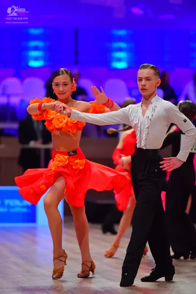 Dancesport competitor: Female dancer: bright orange two-piece Latin dance outfit featuring a crop top a