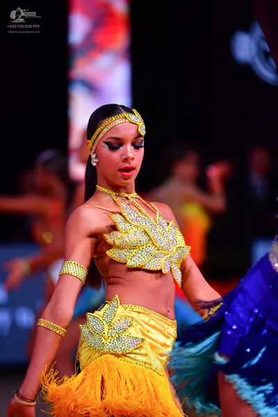 Dancesport competitor: Female dancer in foreground: yellow two-piece Latin dress with silver sequin lea