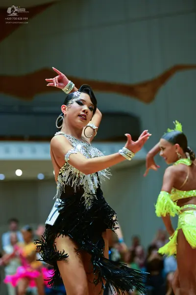 Dancesport competitor: Female dancer in foreground: black Latin dress with a silver/white sequined top 