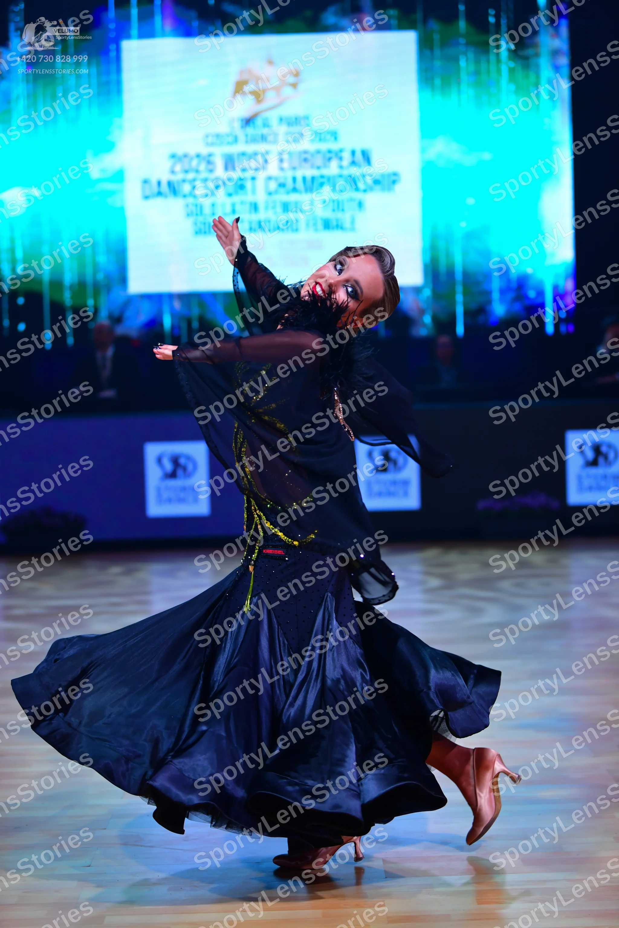Dancesport competitor: Female dancer: dark blue ballroom dress with a sheer top featuring gold/yellow s