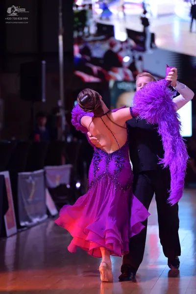 Dancesport competitor: Female dancer: purple Latin dress with sequin embellishments and a large purple 
