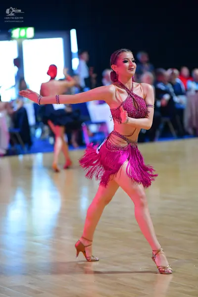 Dancesport competitor: Female dancer in foreground: magenta Latin dress with a sequined halter-style to