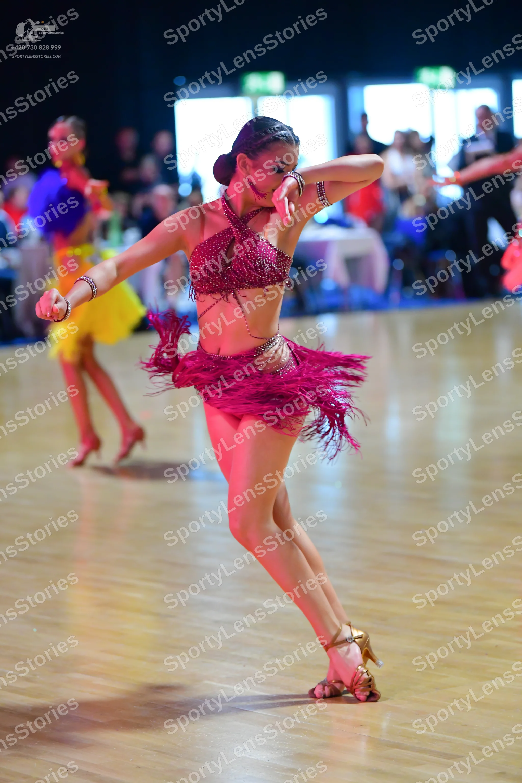 Dancesport competitor: Female dancer (foreground): magenta two-piece Latin costume with a sequined top