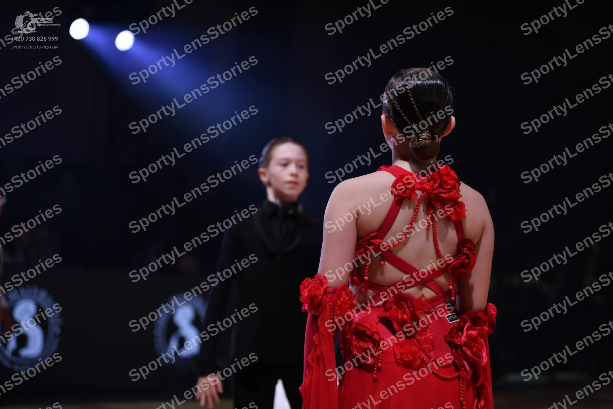 Dancesport competitor: Female dancer in foreground: red latin dress with red floral embellishments on t