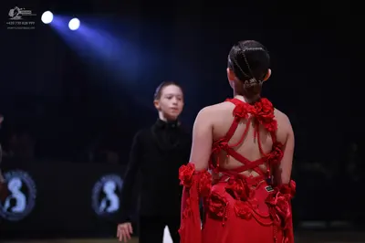 Dancesport competitor: Female dancer in foreground: red latin dress with red floral embellishments on t