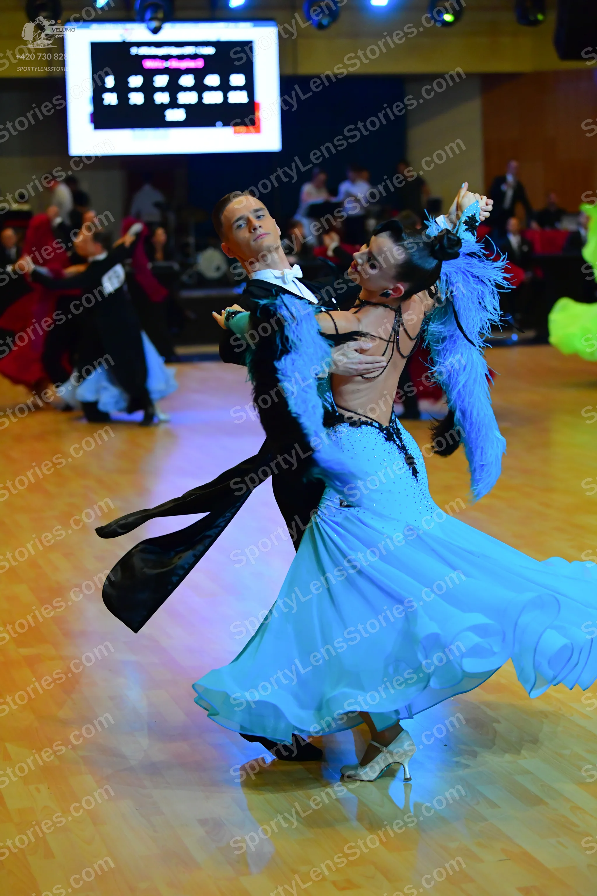Dancesport competitor: Main female dancer: light blue flowing dress with a lace bodice and large blue f