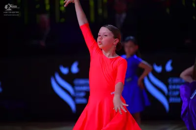 Dancesport competitor: Female dancer in foreground: bright orange long-sleeved Latin dress in a smooth,