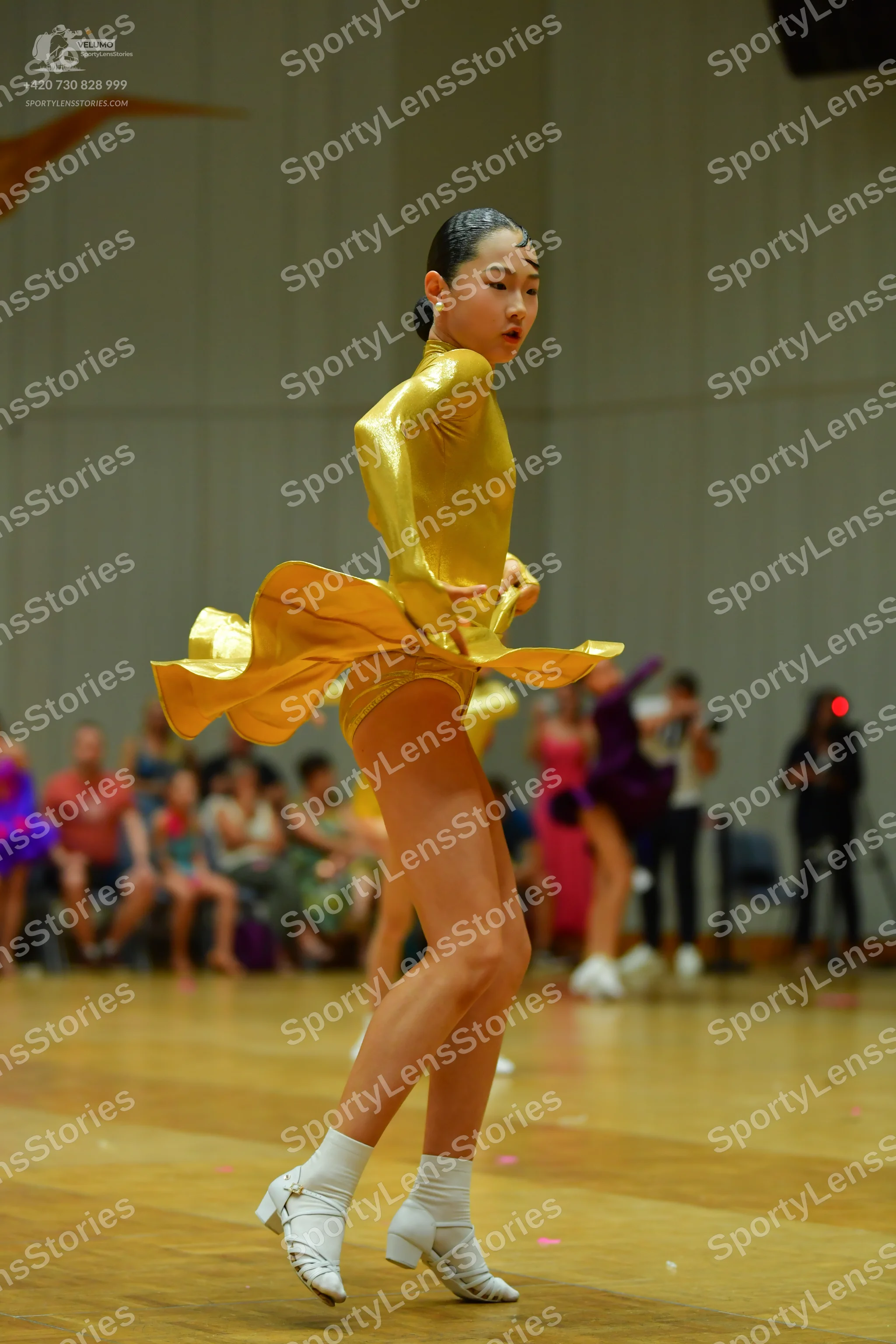 Dancesport competitor: Female dancer in foreground: gold satin Latin dress with long sleeves and a flar