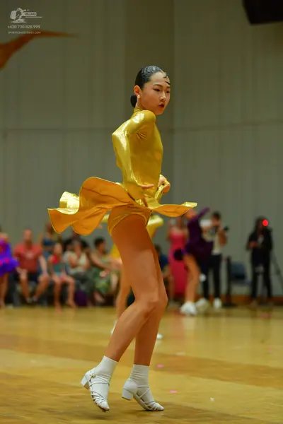 Dancesport competitor: Female dancer in foreground: gold satin Latin dress with long sleeves and a flar