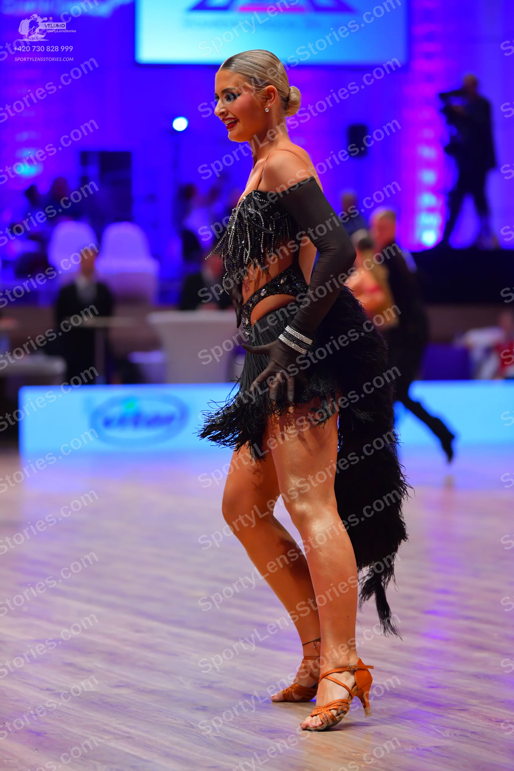 Dancesport competitor: Female dancer: black Latin dress with long sleeves, fringe, and cutouts