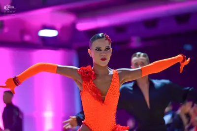 Dancesport competitor: Female dancer: bright orange sequined Latin dress with long matching orange glov