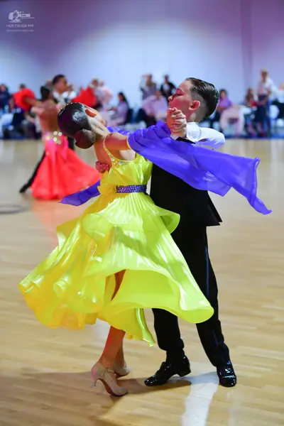 Dancesport competitor: Female dancer in foreground: yellow latin dress with a flowing skirt and a purpl