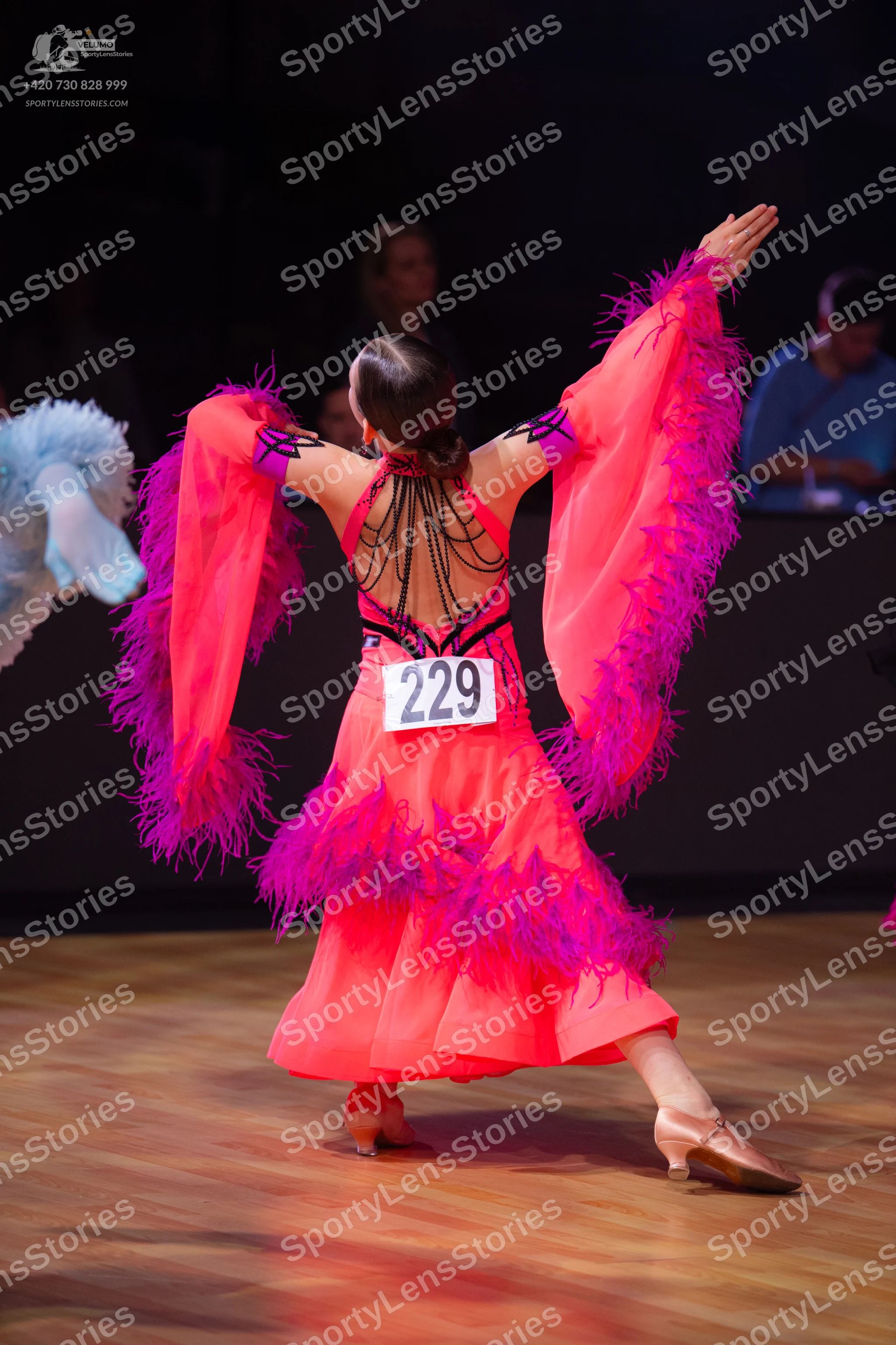 Dancesport competitor: Female dancer: bright pink Latin dress with large, flowing, fringed sleeves and 