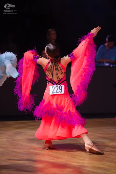Dancesport competitor: Female dancer: bright pink Latin dress with large, flowing, fringed sleeves and 