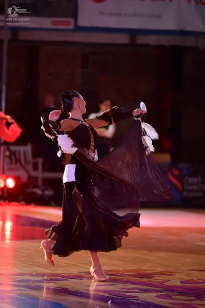 Dancesport competitor: Female dancer: black ballroom dress with sheer, lace-like sleeves and a large, f
