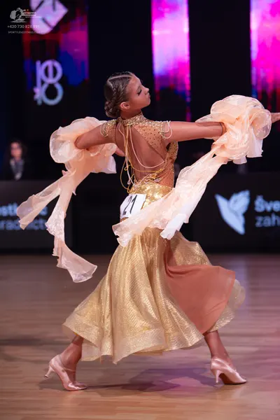 Dancesport competitor: Female dancer: gold/champagne latin dress with shimmering fabric, featuring larg