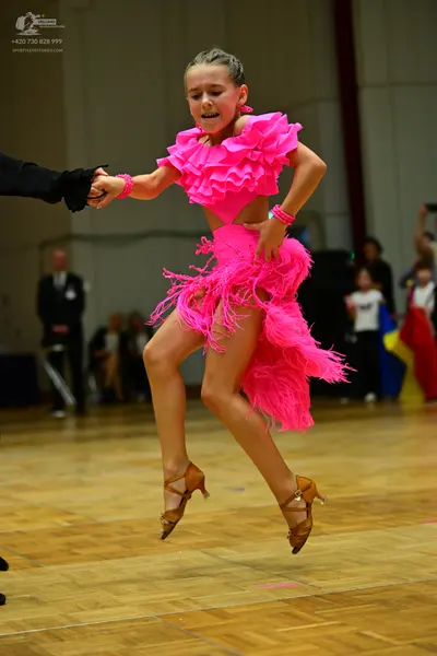 Dancesport competitor: Female dancer: bright pink Latin dance dress with many ruffles, fringe, and matc