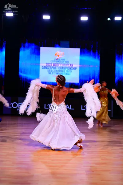 Dancesport competitor: Female dancer in foreground: white dress with large white feathery arm accessori
