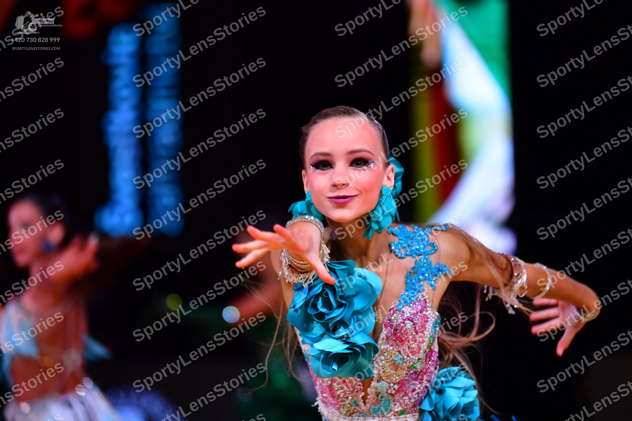 Dancesport competitor: Female dancer (foreground): light blue and white latin dress with large blue fab