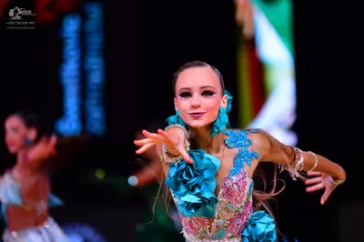 Dancesport competitor: Female dancer (foreground): light blue and white latin dress with large blue fab