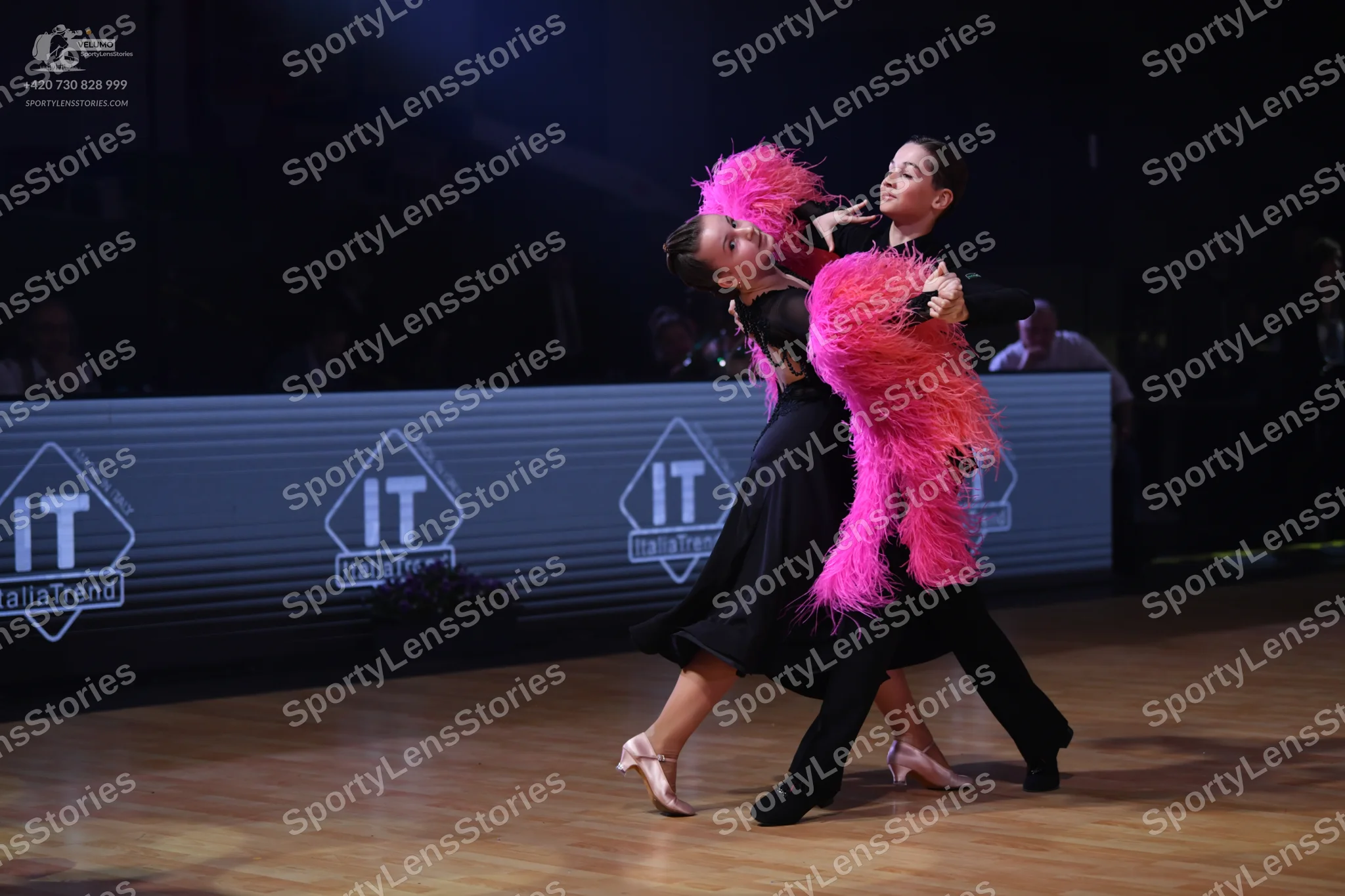 Dancesport competitor: Female dancer: black Latin dress with large, voluminous pink feather accents