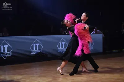 Dancesport competitor: Female dancer: black Latin dress with large, voluminous pink feather accents