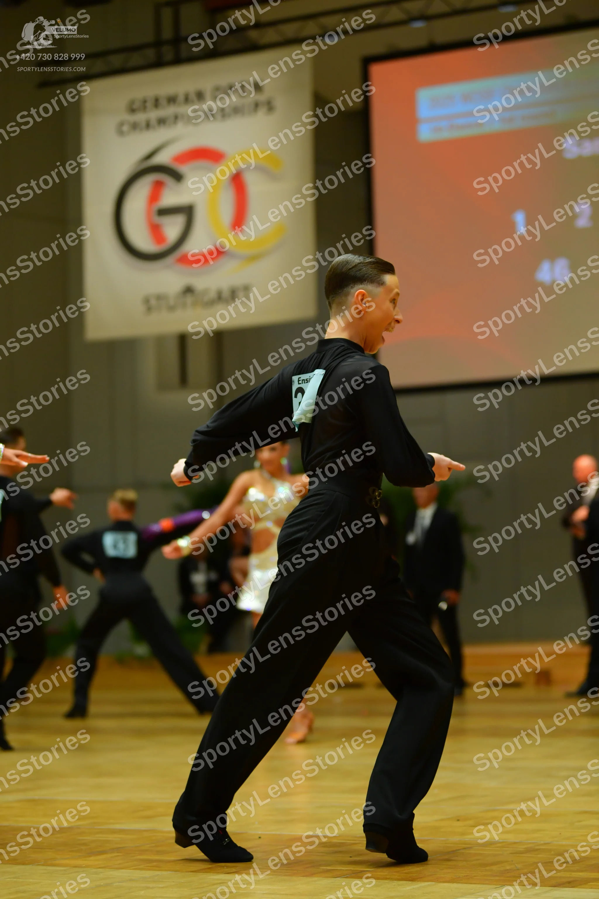 Dancesport competitor: Male dancer in foreground: black long-sleeved shirt and black trousers