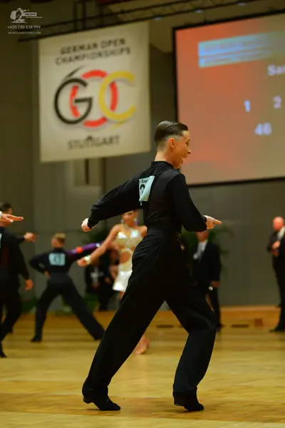 Dancesport competitor: Male dancer in foreground: black long-sleeved shirt and black trousers