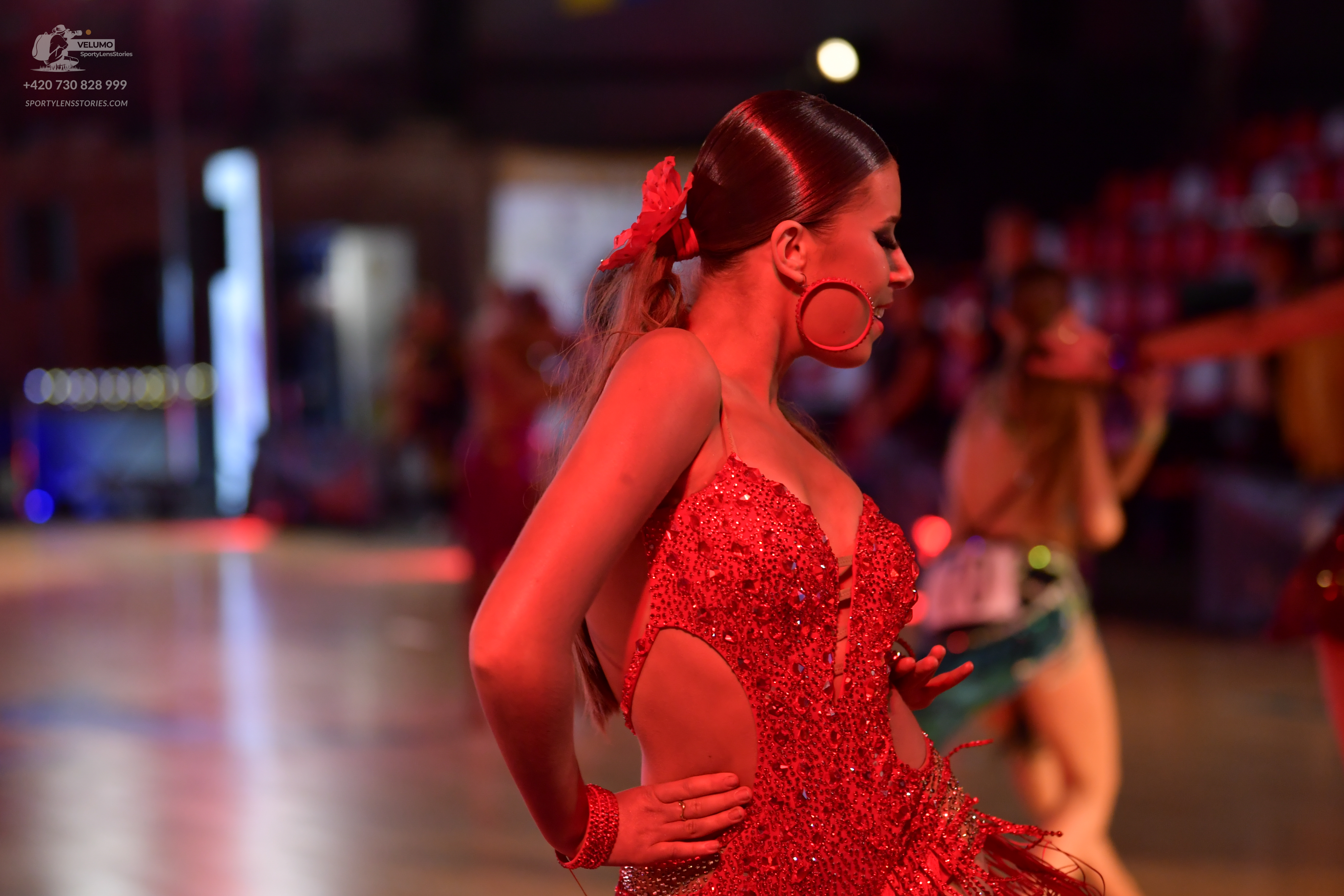 Dancesport competitor: Female dancer in foreground: red latin dress with sequins and cutouts
